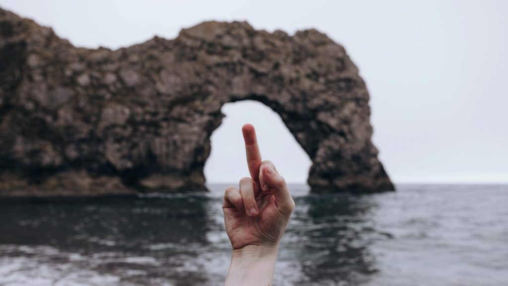 person showing right middle finger on front of brown rock formation
